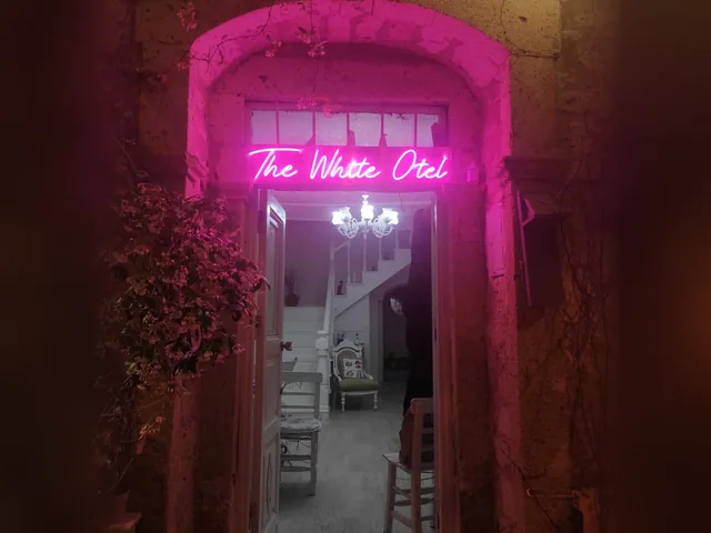 Taş kemerli girişte pembe neon yazı: The White Otel